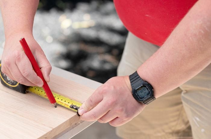 A Bunnings team member marking a piece of timber with measuring tape and a pencil