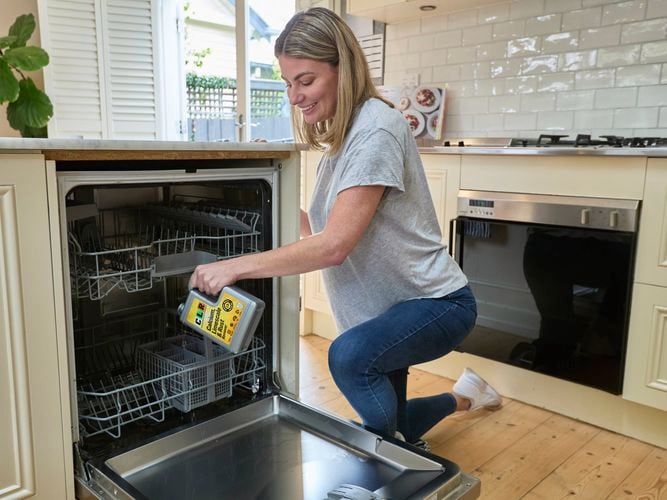 A lady holding a bottle of CLR Calcium Limescale & Rust 1L in a Dish Washer in a kitchen.