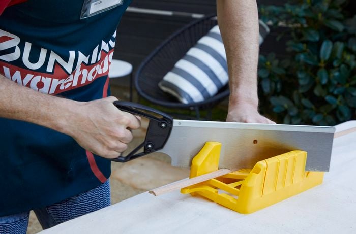 Person using mitre box to cut dowel with a handsaw.