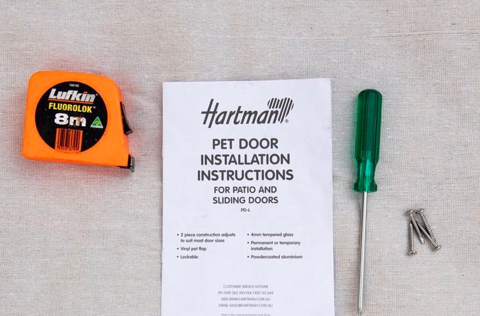 Measuring tape, pet door installation instruction booklet and screwdriver on table top.