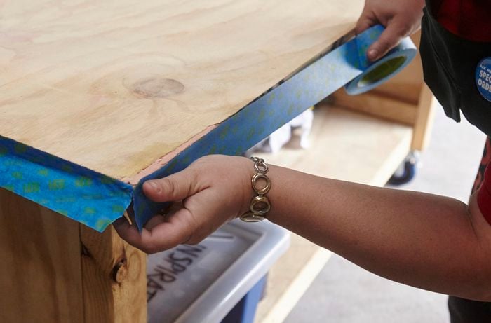 A person sticking masking tape to the edge of a plywood benchtop