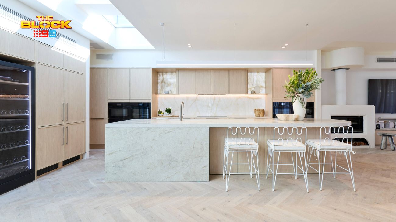 Contemporary kitchen featuring a large marble-look island bench, light timber cabinetry, white bar stools and skylights.