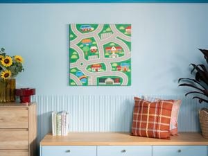 A light blue room with a map-themed wall art piece above a low cabinet decorated with books, pillows, plants, and sunflowers in a vase.
