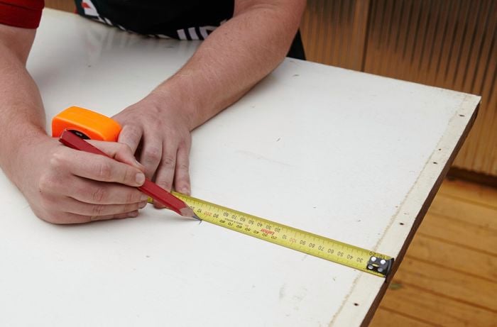 A person marking length on a timber door using a measuring tape and pencil