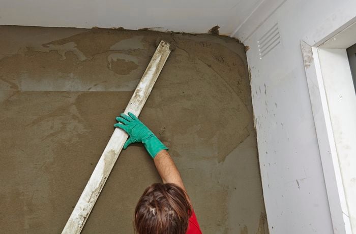 A person screeding a plastered wall with a straight edge