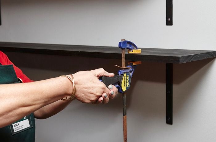 A person clamping a shelf to a wall bracket