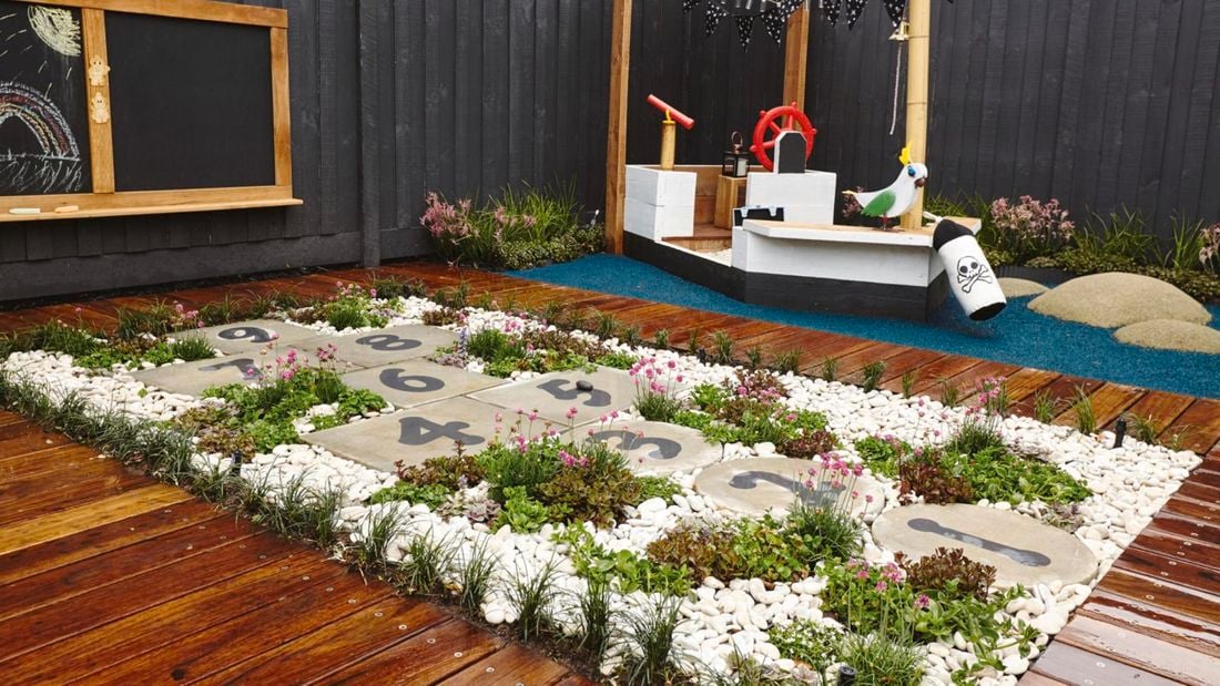 An outdoor play area with round hopscotch pavers set into pebbles surrounded by timber decking