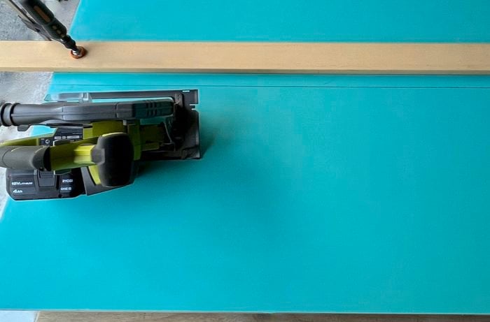 A blue door panel clamped to a table, with a circular saw on top of it.