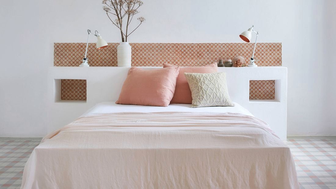 A modern bedroom featuring a built-in white headboard with decorative terracotta tiles, displaying the latest tile trends for stunning and functional spaces.
