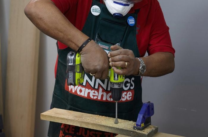 A person drilling a hole into a length of timber clamped to a work bench