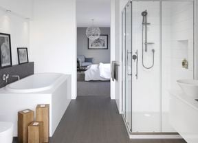 A white bathroom with dark grey slate floor opening off a bedroom