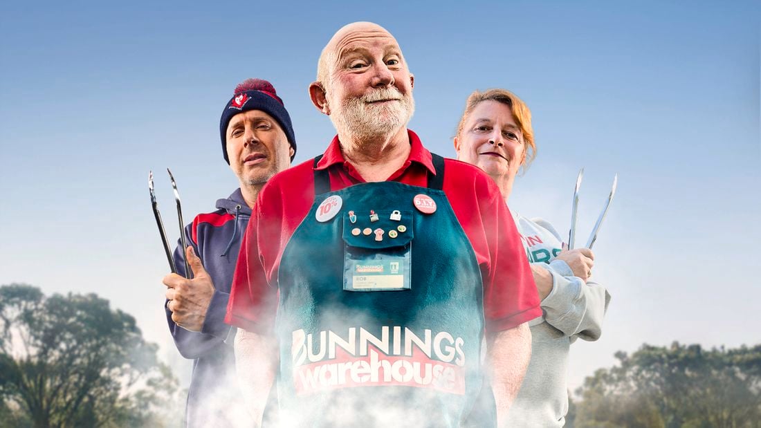 A Bunnings Team Member and 2 people in front of a BBQ with food on top of it.