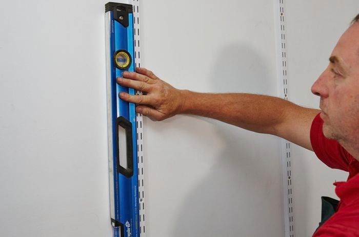 A spirit level being used to ensure the straightness of mounting tracks for shelving