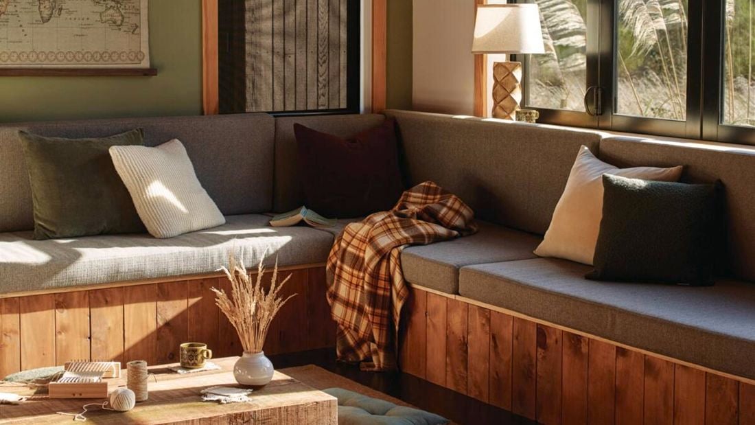 <p>Grey couch with grey curtains by the open window in a living room. Other furnishings like a coffee table, a white lamp and a large window are also featured</p>