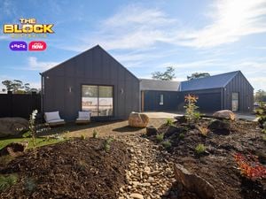 The front area of a house with rocks, shrubs, a driveway and a timber fence in it.