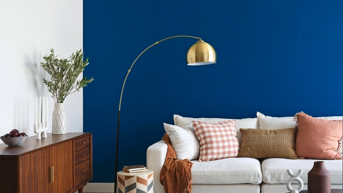 A living room with a navy blue wall, couch, buffet table and rug.