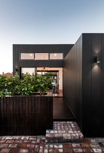 Exterior view of a modern two-storey house with dark grey timber cladding and a pathway and fence of decking timber
