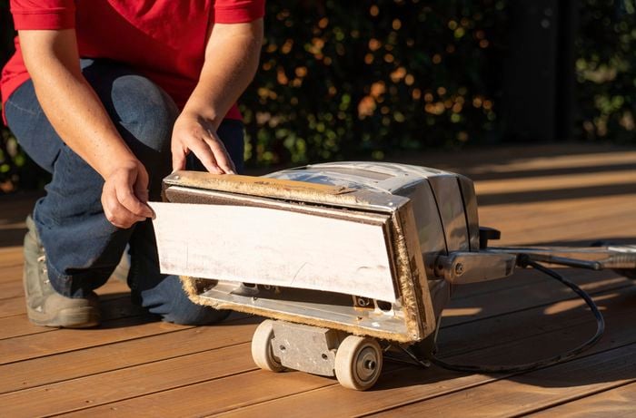 A close-up of a person replacing the sanding belt on a drum floor sander to move to a finer grit stage for a smoother timber deck finish.