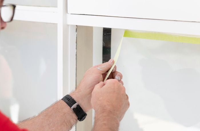 A person removes the yellow masking tape to admire the quality paint job and now look timber window frames.
