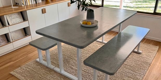 A cement-look dining table in a living room, a vase and two lemons on top of it.