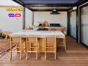 An outdoor area with a kitchen bench, with a pizza oven, barbecue on it and chairs in front of it.