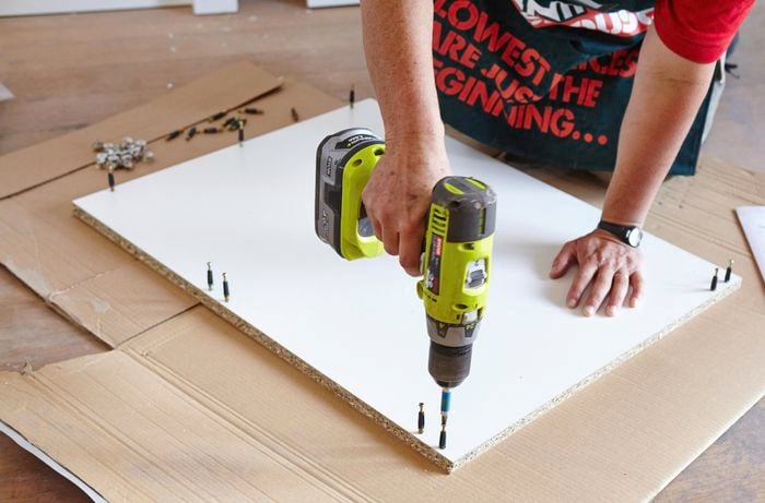 A person inserting pins into a cabinet panel using a cordless drill