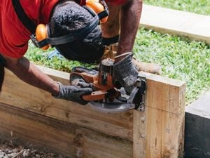 An image showing a tradesperson in PPE with a small circular saw trimming down timber sleepers for a retaining wall