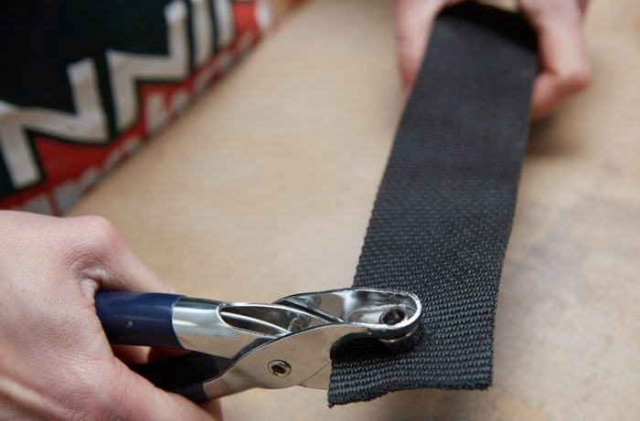 A person using a crimping tool to crimp eyelets in a length of webbing 