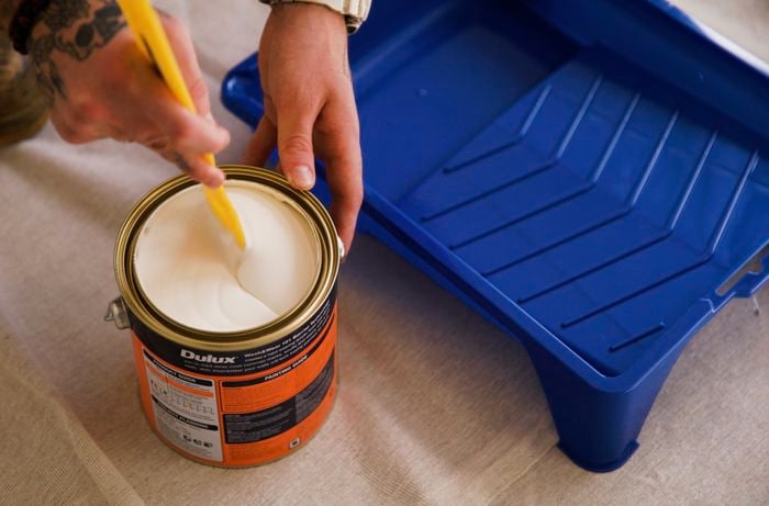 A hand with a tattoo is mixing Dulux paint using a brush, while a paint tray is kept on the side.