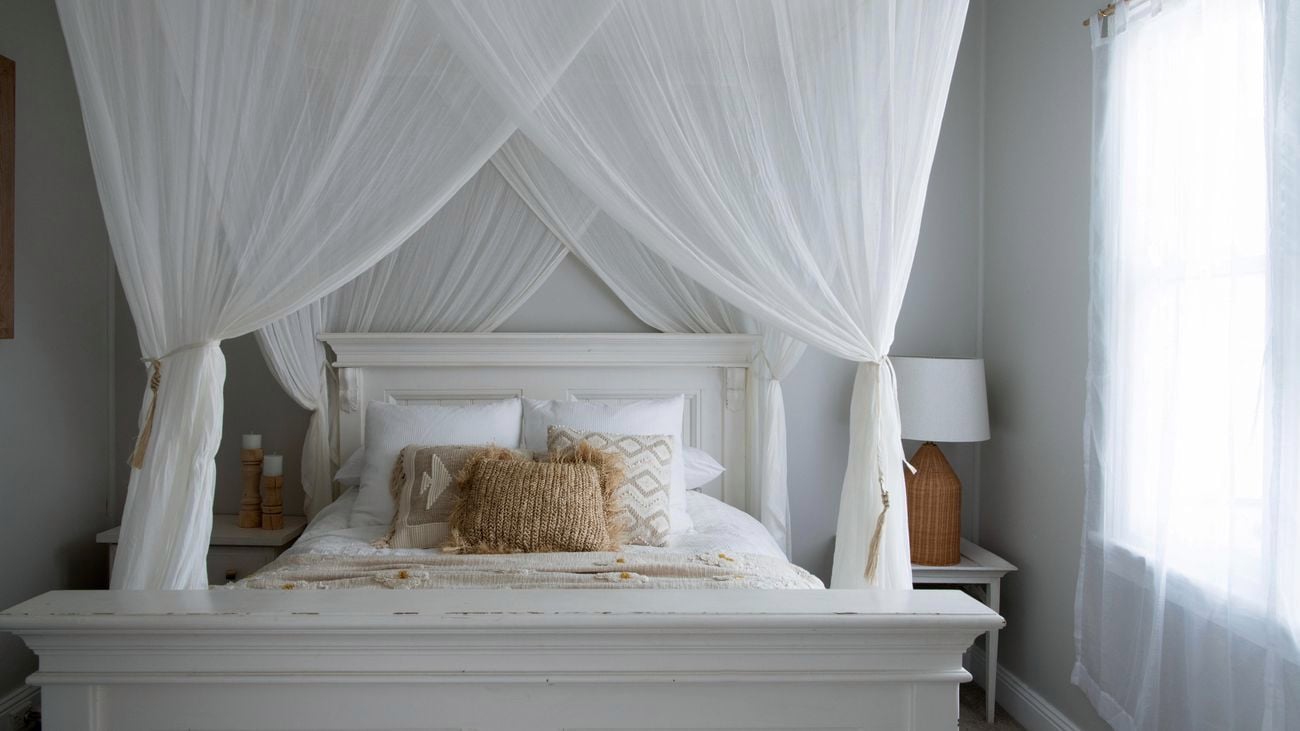 A white canopy hanging above a timber bed with natural textured accessories