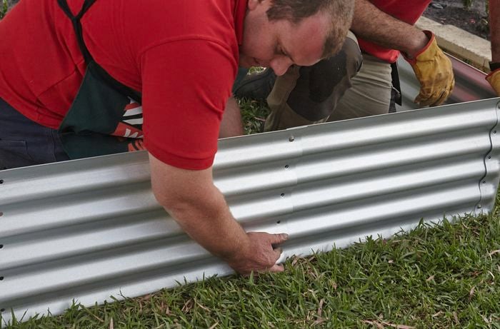 Person putting sides of corrugated iron garden bed in place.