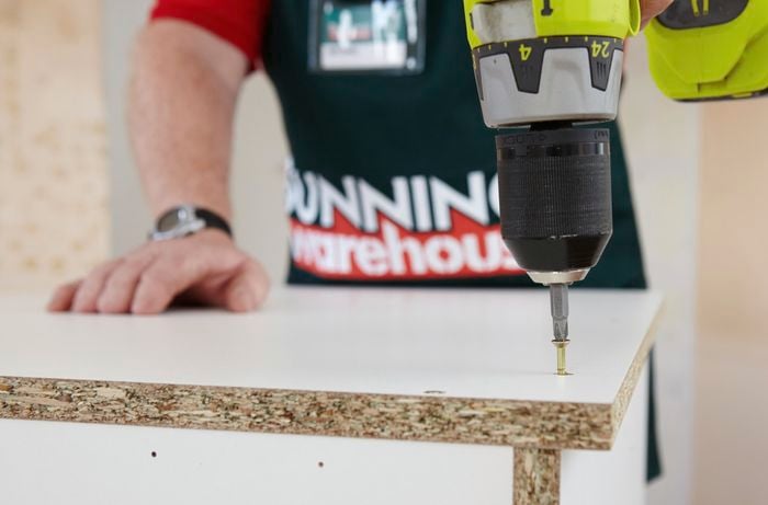Person using a cordless driver to attach two cabinet panels