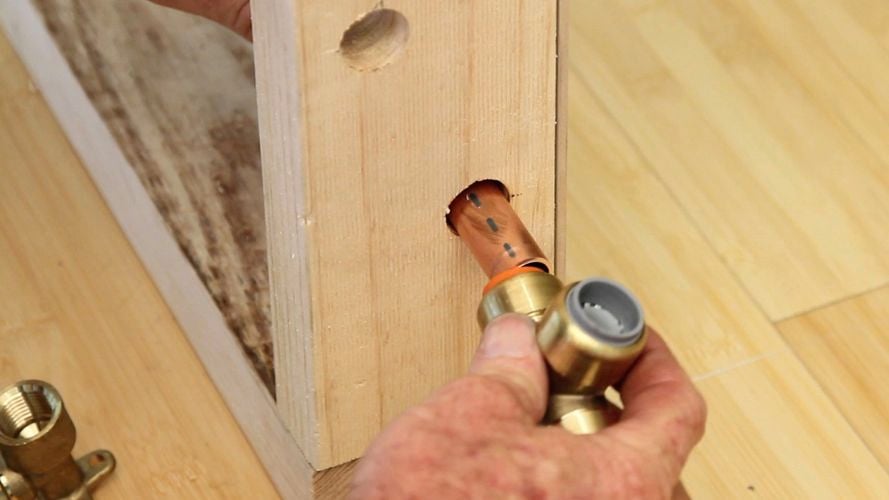 A person connecting a brass tee to a copper bar.