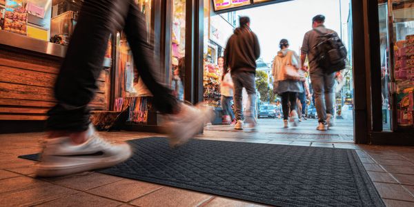 Commercial entrance mat at a busy retail doorway with people walking across it