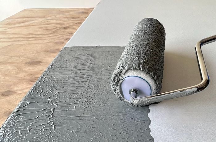 Close up of a paint roller applying grey paint to a door panel.
