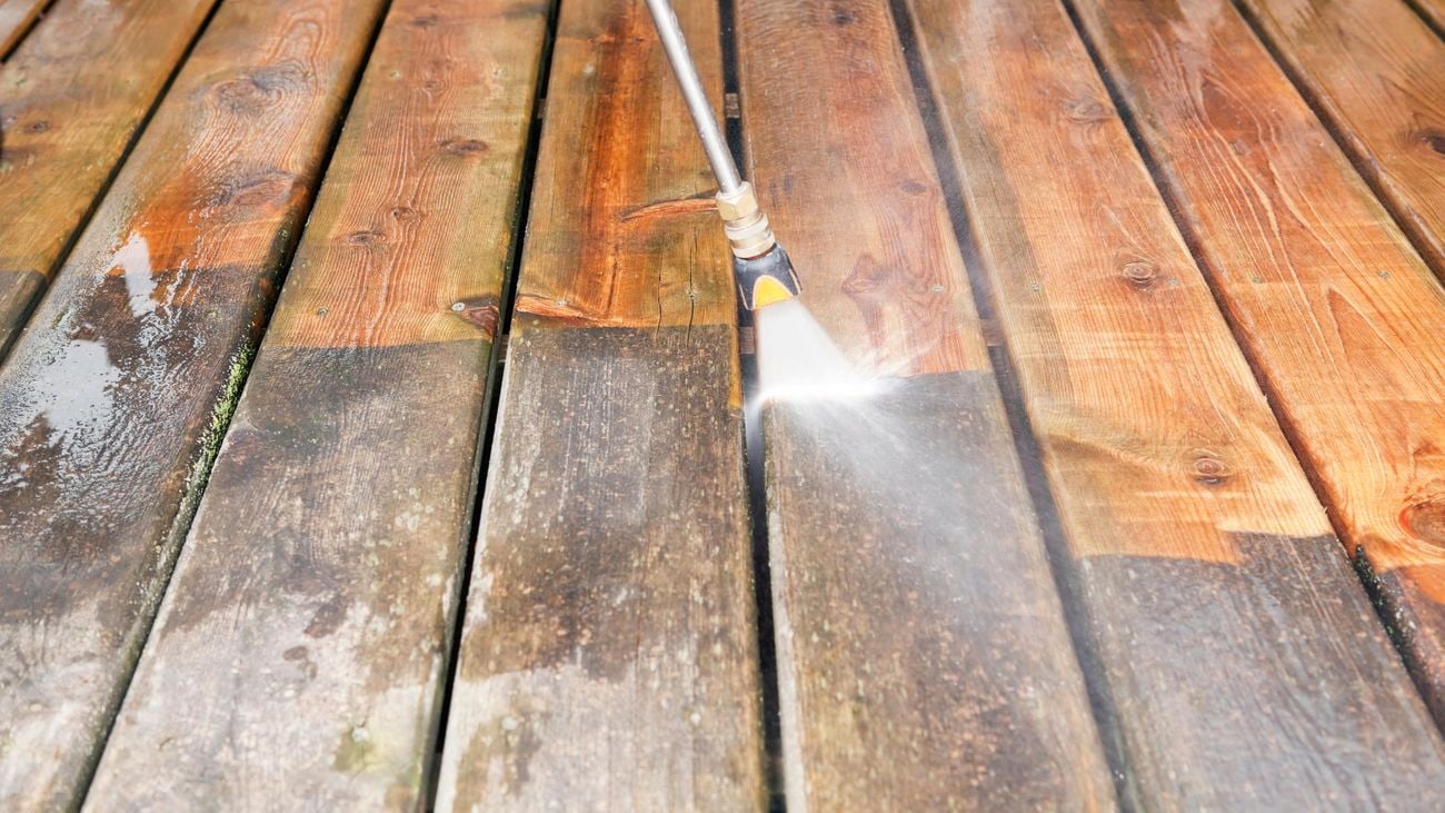 A pressure washer spraying a weathered wooden deck, with half the deck clean