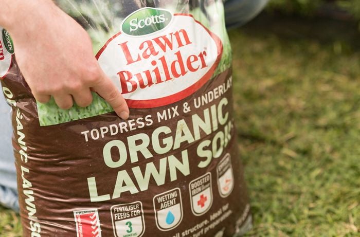 A person is pointing to a bag of topdress mix and underlay for lawn care.