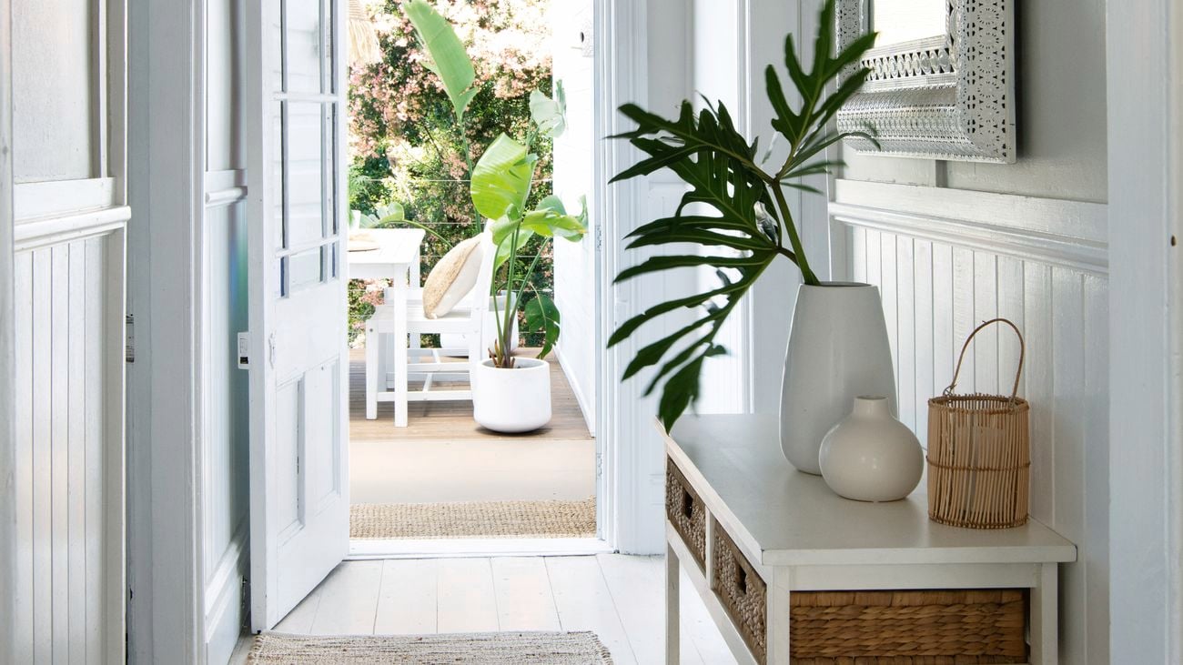 A bright white hallway with panelled walls leads out to an outdoor room set up on a deck