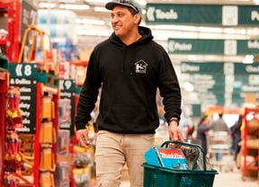 customers walking through a Bunnings store,  carrying a bunnings shopping basket with items in it.