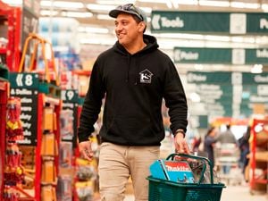 customers walking through a Bunnings store,  carrying a bunnings shopping basket with items in it.