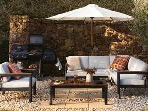 An outdoor setting a BBQ and an umbrella outdoors on paved area with pebble stones in it.