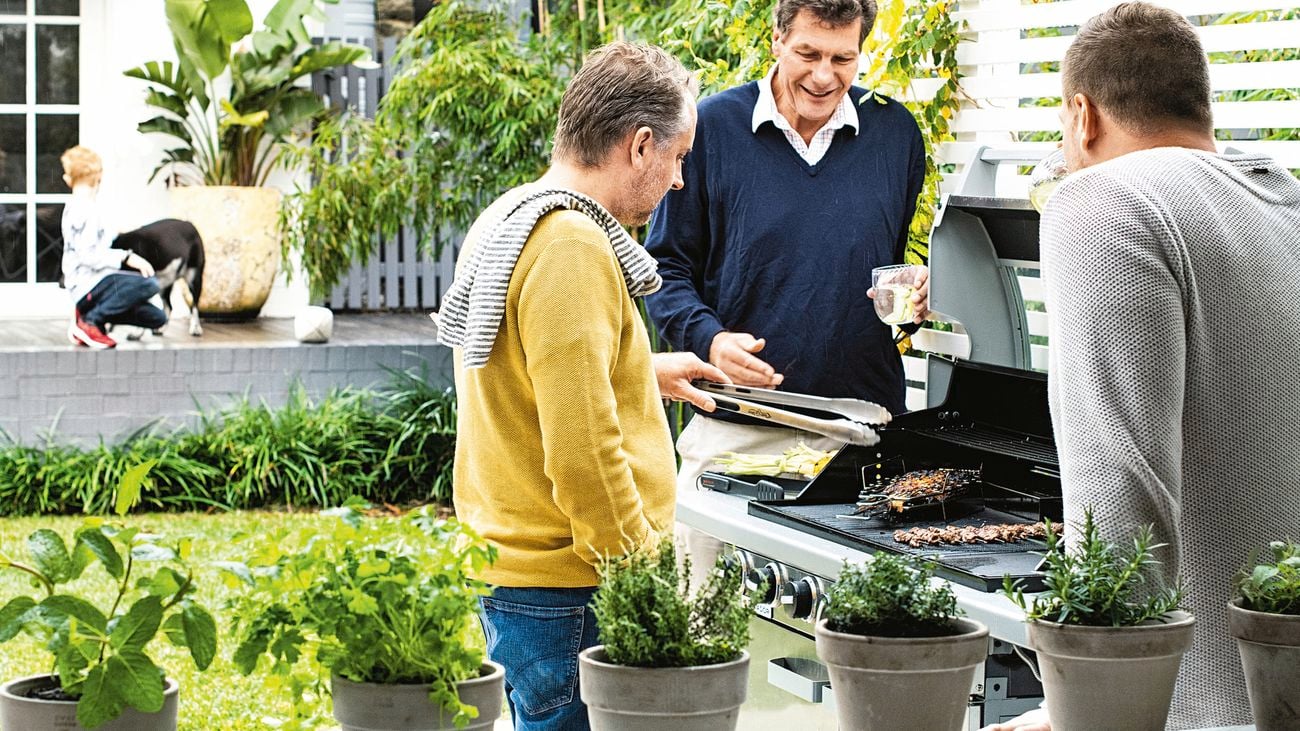 Three men stand around a bbq while food cooks