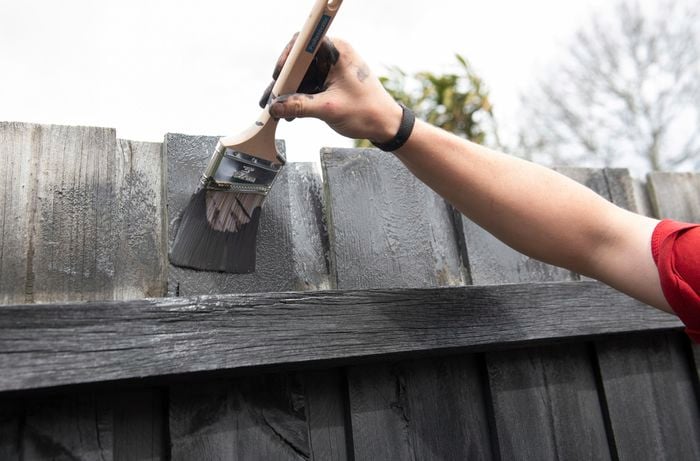 Person painting the top of a fence with a paint brush