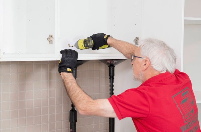 A Bunnings Team Member is using a power drill to unscrew and remove a wall cabinet.