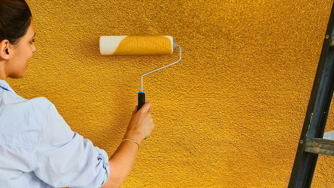 Using a paint roller to paint an external wall yellow