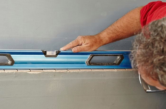 A spirit level being used to ensure that a row of mosaic tiles are level before applying tile adhesive