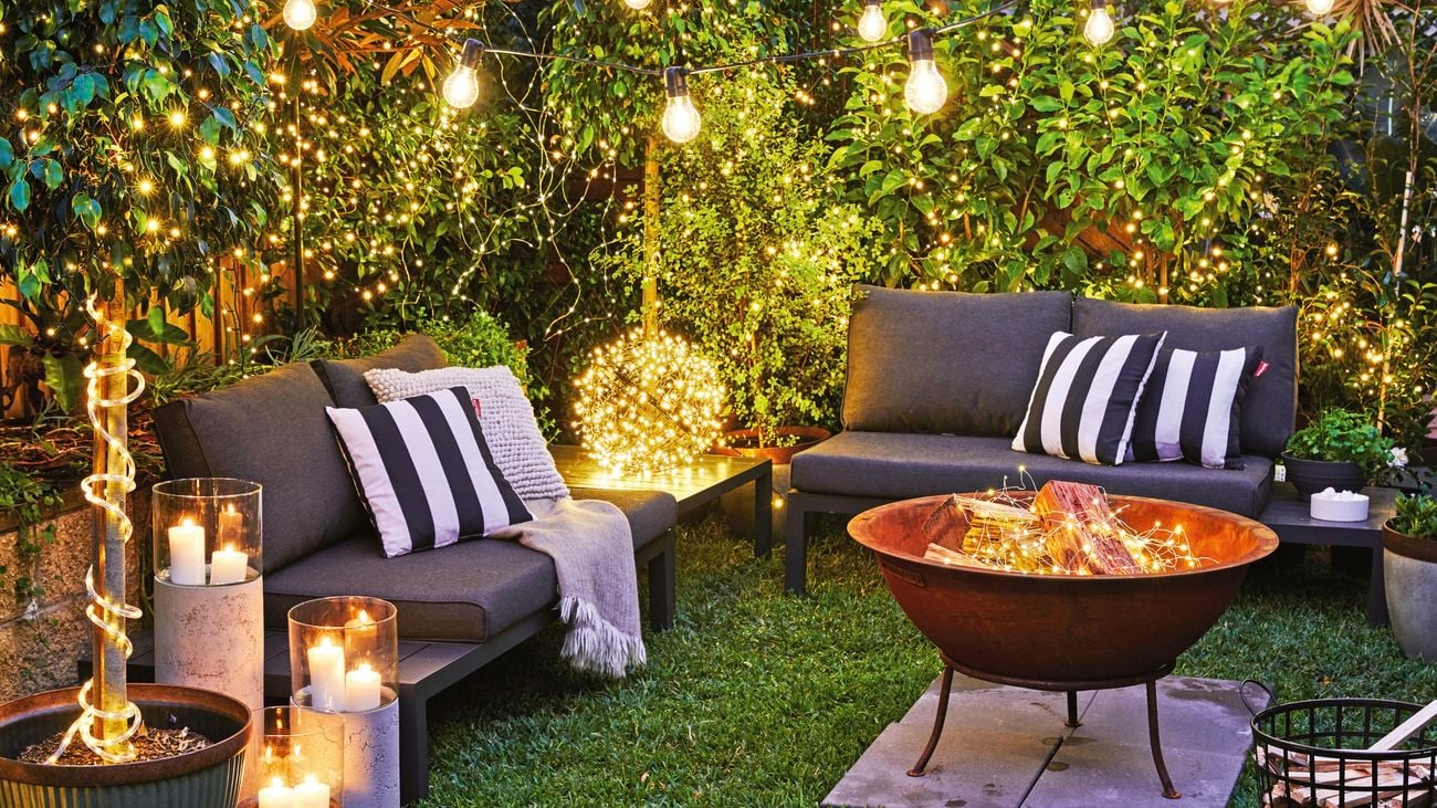 Outdoor furniture placed around an outdoor fire pit with black and white striped cushions on top of turf.