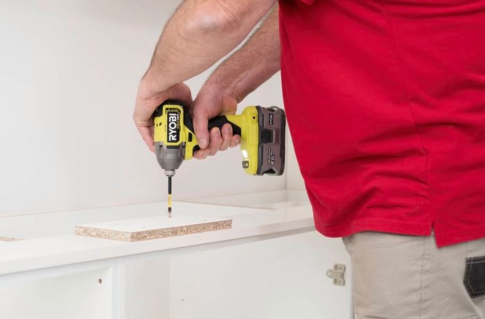 A person in a red t-shirt is using a drill to join kickboards using a backing brace.
