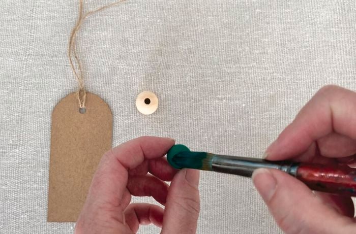 Hands using paintbrush to paint macrame bead green