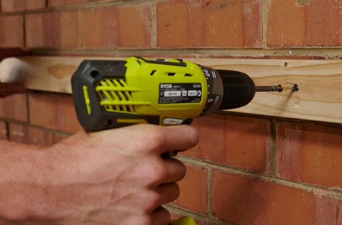 A wooden length being screwed into a brick wall